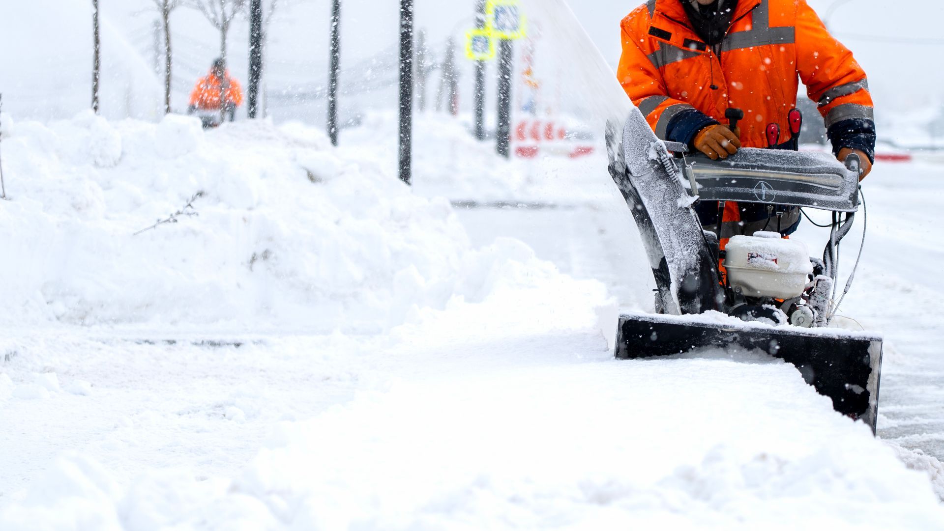 Commercial snow removal services in action with snowblower truck during heavy blizzard. Snow removal services clearing sidewalks with a snow blower during a heavy winter snowstorm.