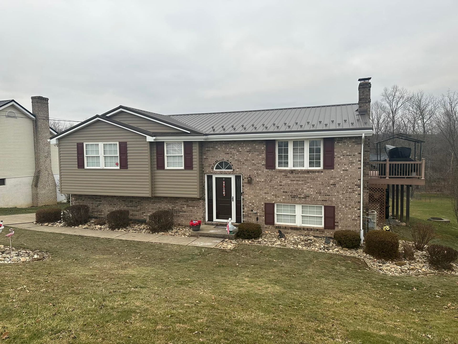 A large brick house with a metal roof is sitting on top of a lush green field.