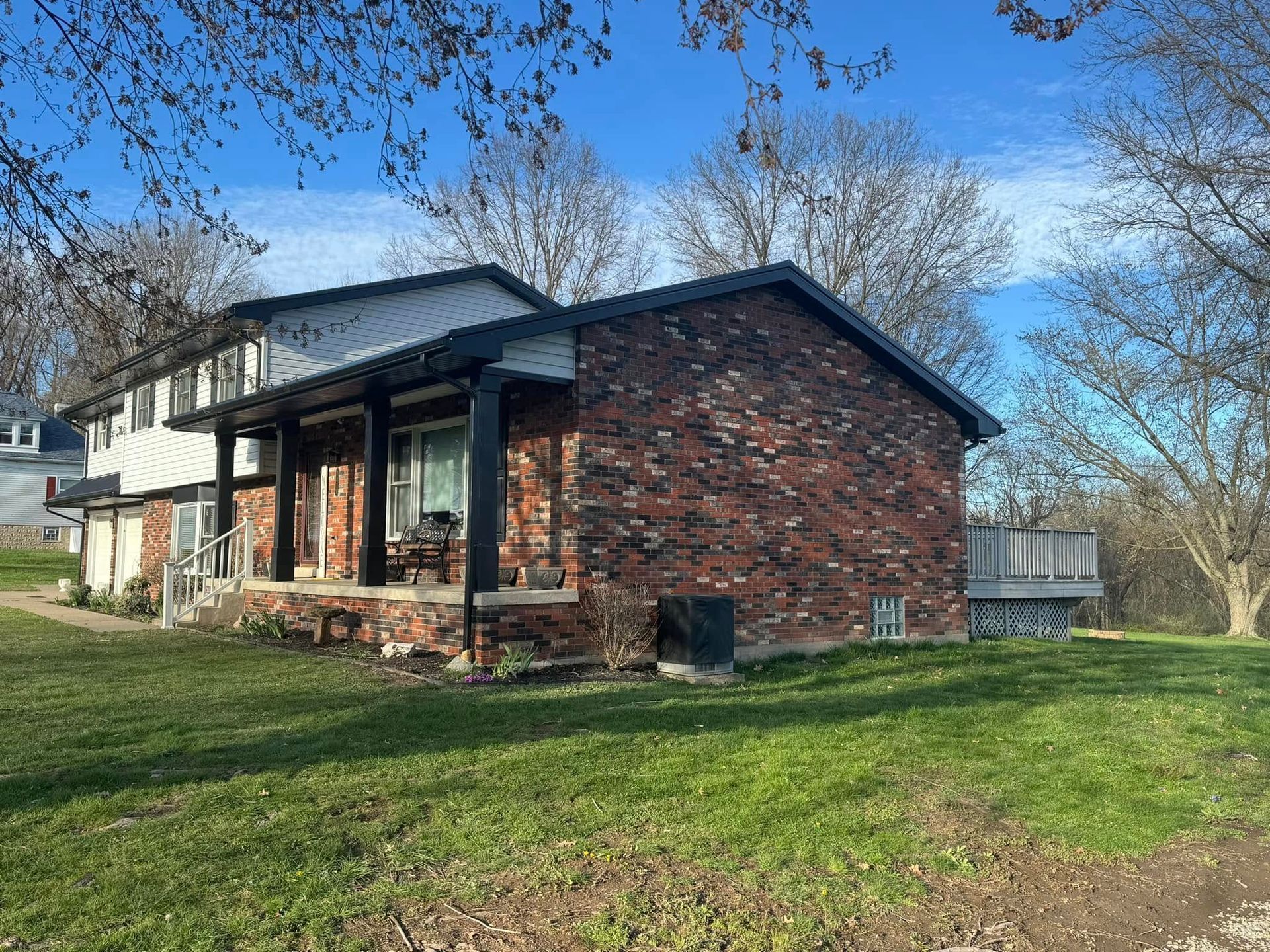 A brick house with a porch and a large lawn in front of it.
