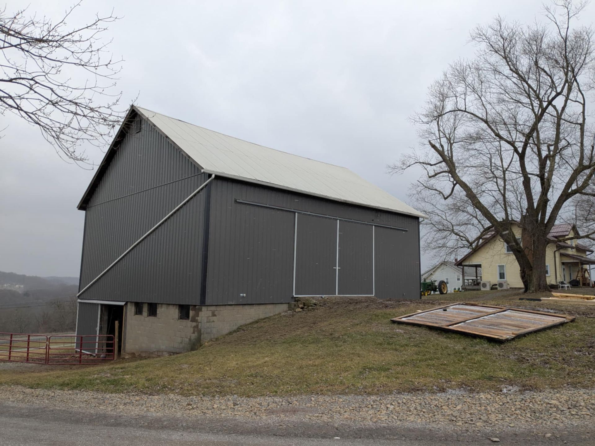 A gray barn with a white roof is sitting on top of a grassy hill.