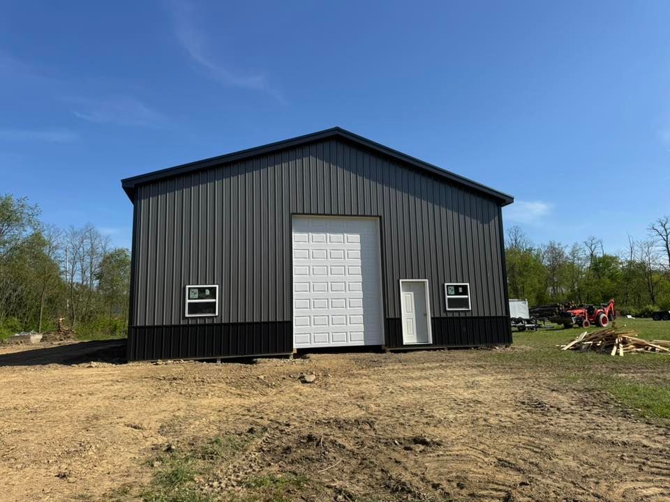 A large metal building with a white door is sitting in the middle of a dirt field.