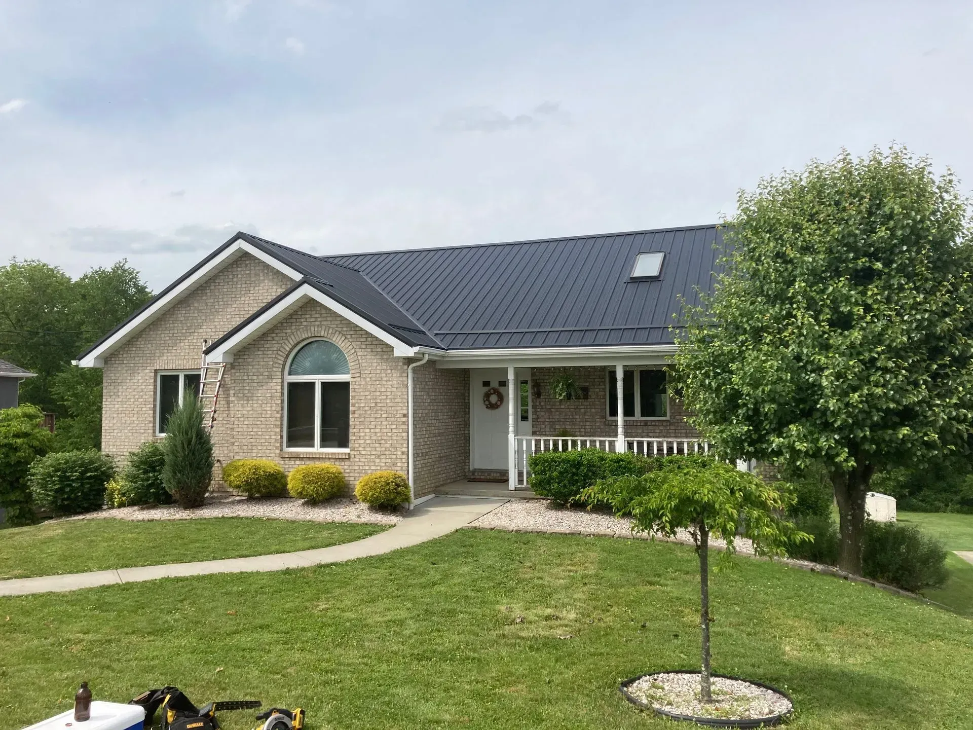 Tan brick house with a dark blue metal roof, white trim, and a small front porch, on a green lawn.