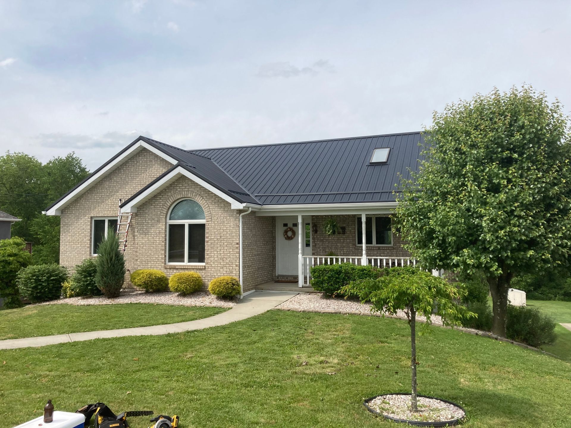 A brick house with a black roof and a large lawn in front of it.