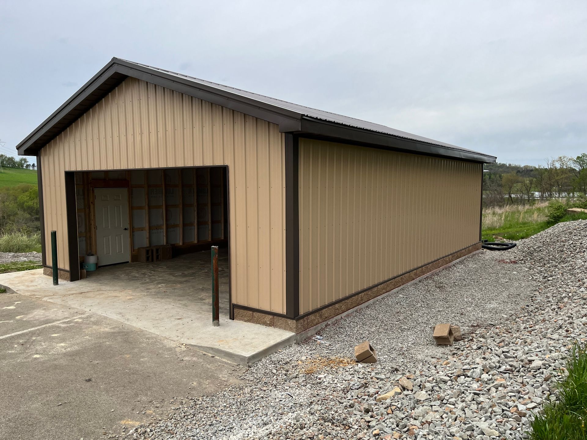 A tan metal garage with a brown roof is sitting on top of a gravel lot.