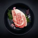 Raw marbled steak on a black plate with green leaves and small pink flowers