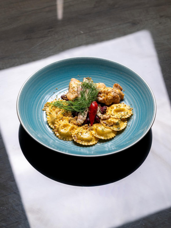 Piatto blu con gnocchi al sugo, broccoli e pollo fritto su un tovagliolo bianco alla luce del sole