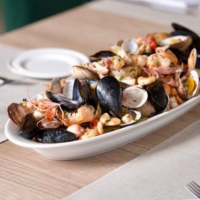 Piatto misto di frutti di mare con cozze, vongole, gamberi ed erbe aromatiche su un piatto da portata bianco.