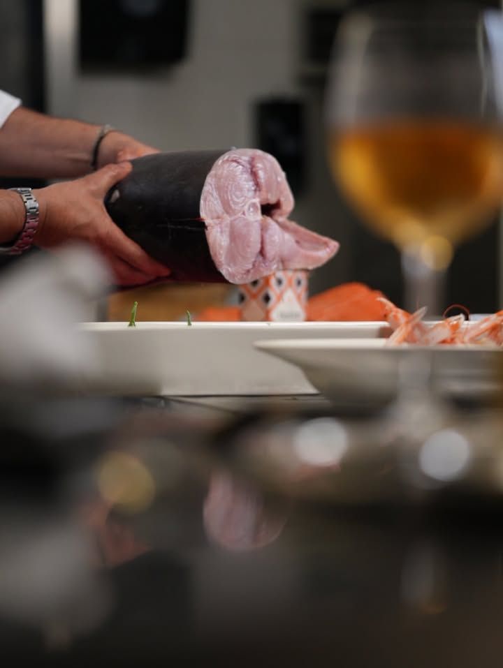 Su un tavolo di ristorante, con mani guantate di nero che dispongono il sushi su un piatto, accanto a un bicchiere di vino.