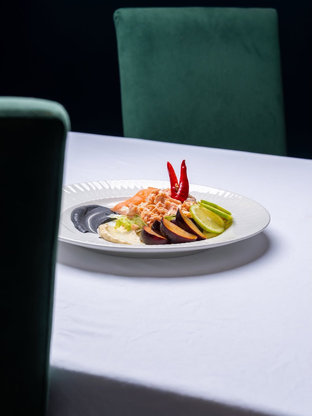 Un piatto bianco con una prelibatezza a base di frutti di mare e peperoni rossi su un tavolo, con sedie verdi sullo sfondo.