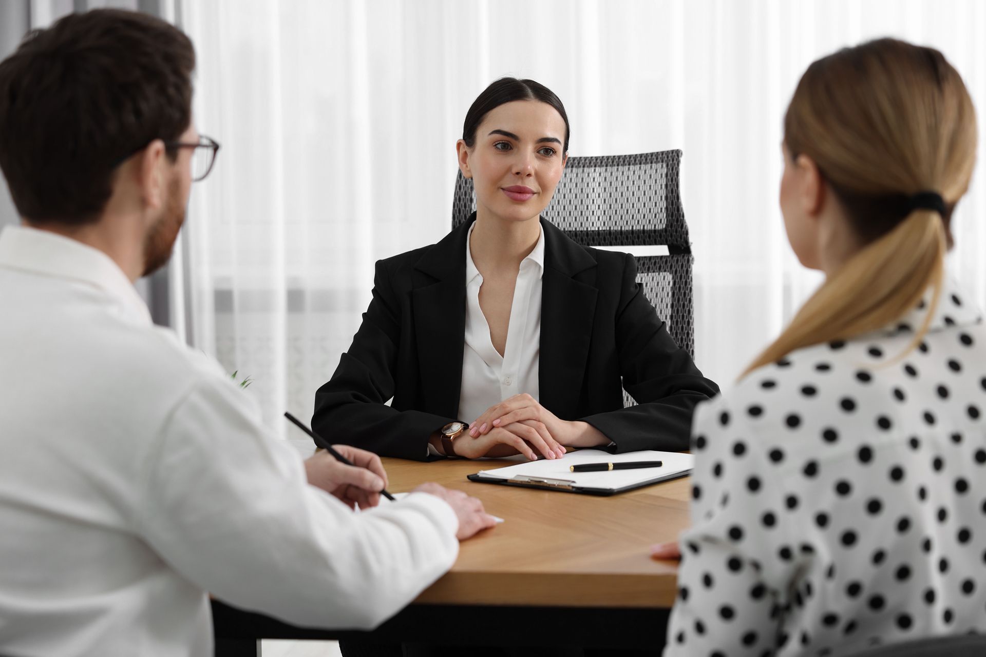 A woman in a blazer sits across from a couple at a desk, likely in a meeting or consultation.