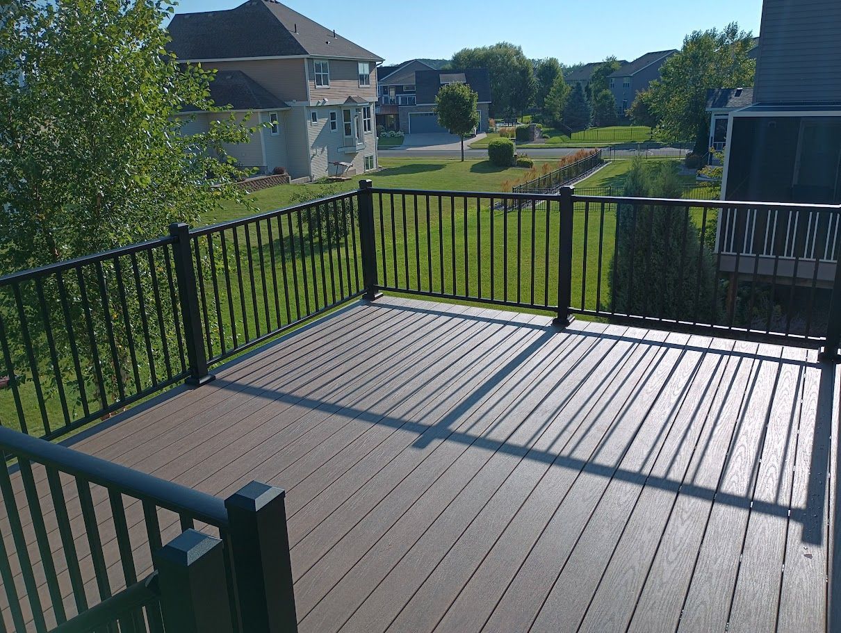 A deck with a black railing and a view of a lush green field.
