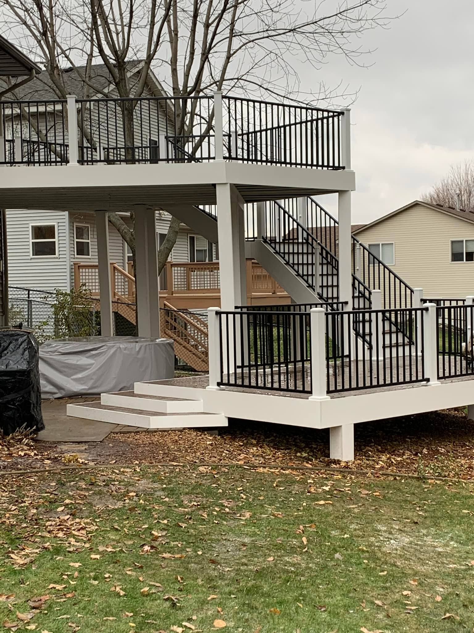 A large deck with stairs leading up to it is in the backyard of a house.