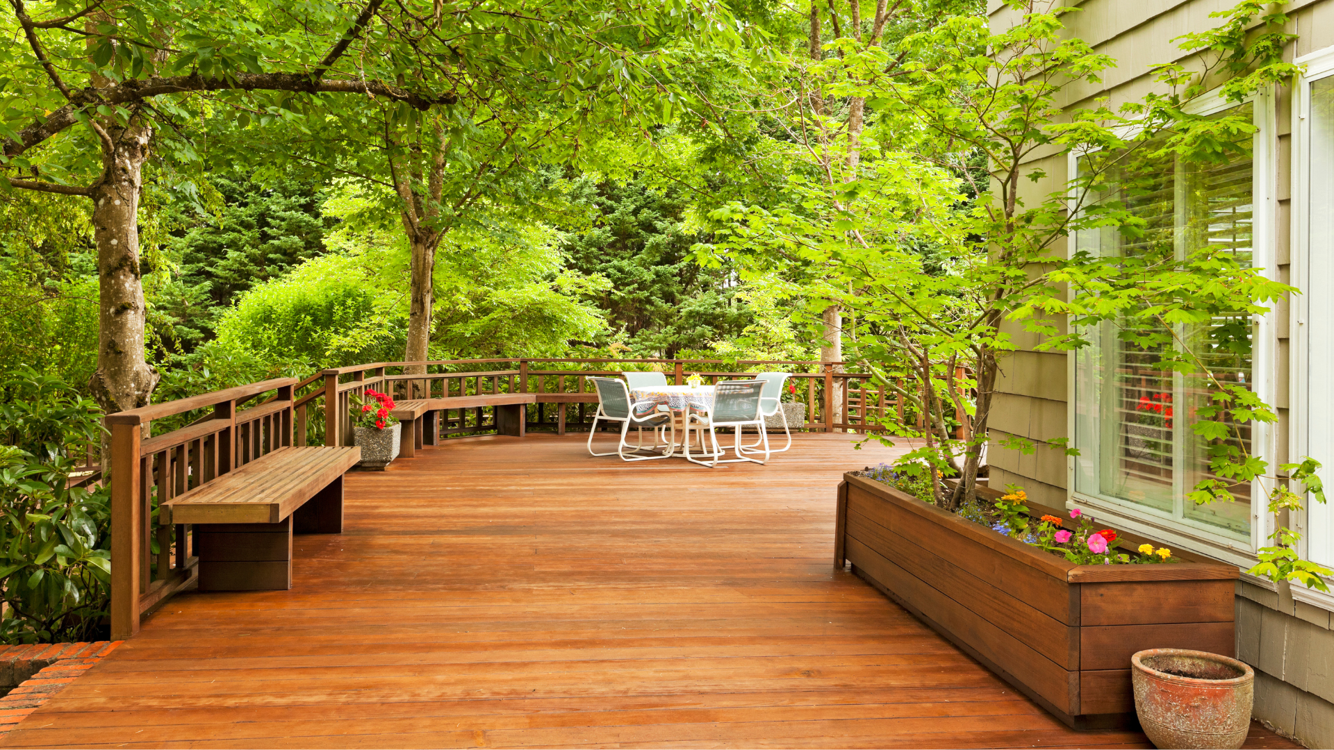 A wooden deck with a table and chairs on it surrounded by trees.