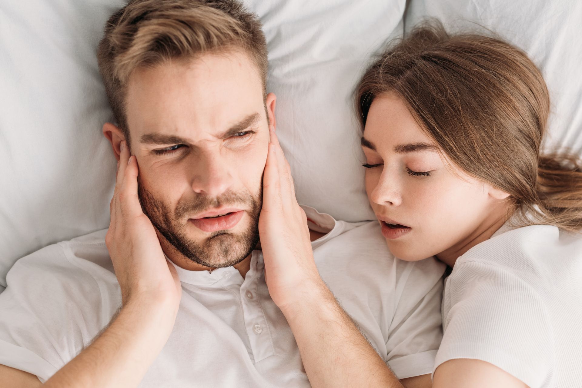 man holding ears laying next to woman snoring | Fix sleep apnea in Lynnwood WA