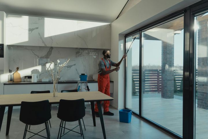 Modern kitchen with island, black stools, and a person cleaning the window beside a patio door.