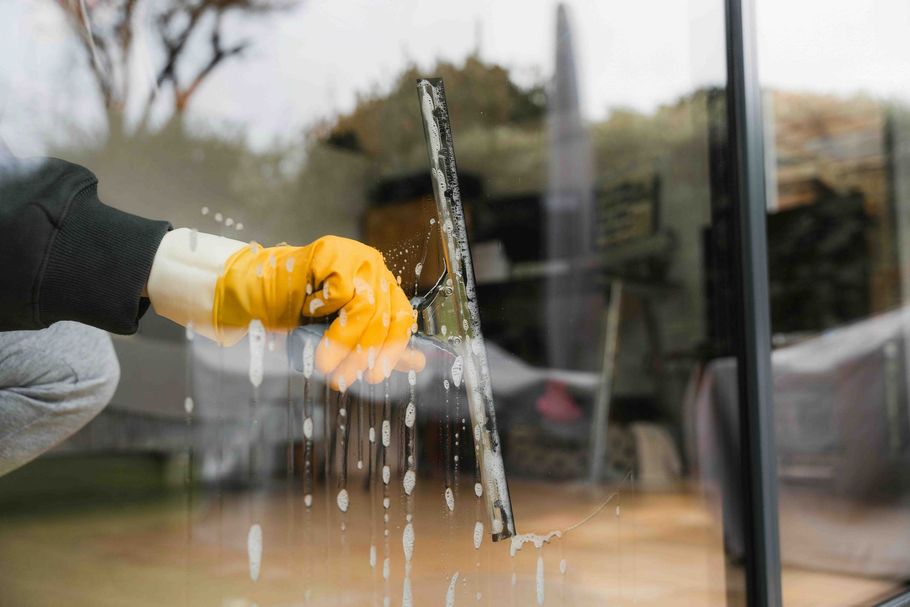 Gloved hand cleaning a glass window with a squeegee, water dripping down the pane