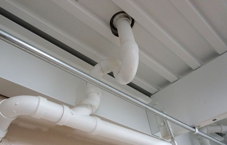 A man is kneeling down and working on a pipe in a room.