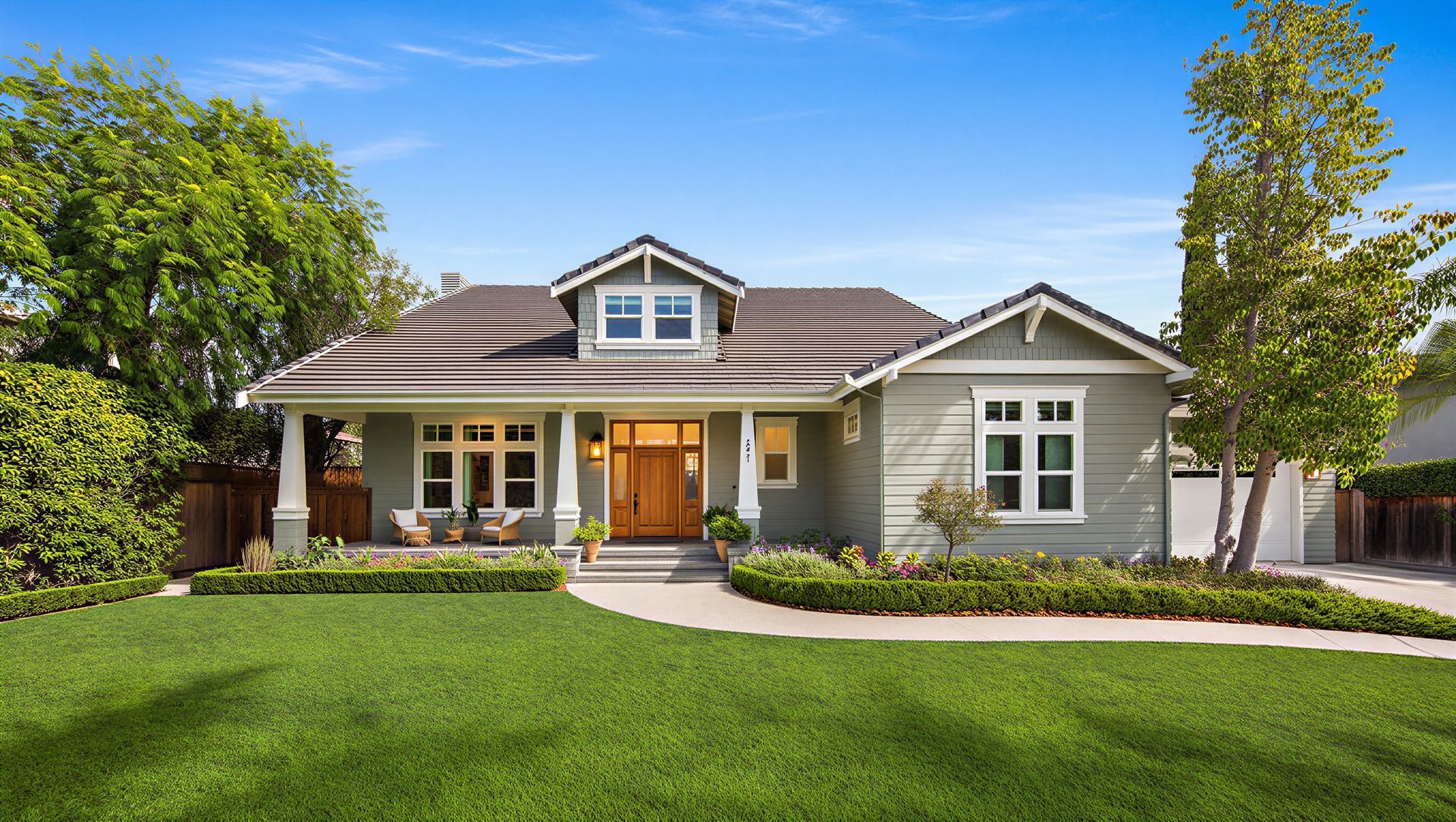 Single-story suburban house with a front porch, gray siding, and a green lawn under a blue sky