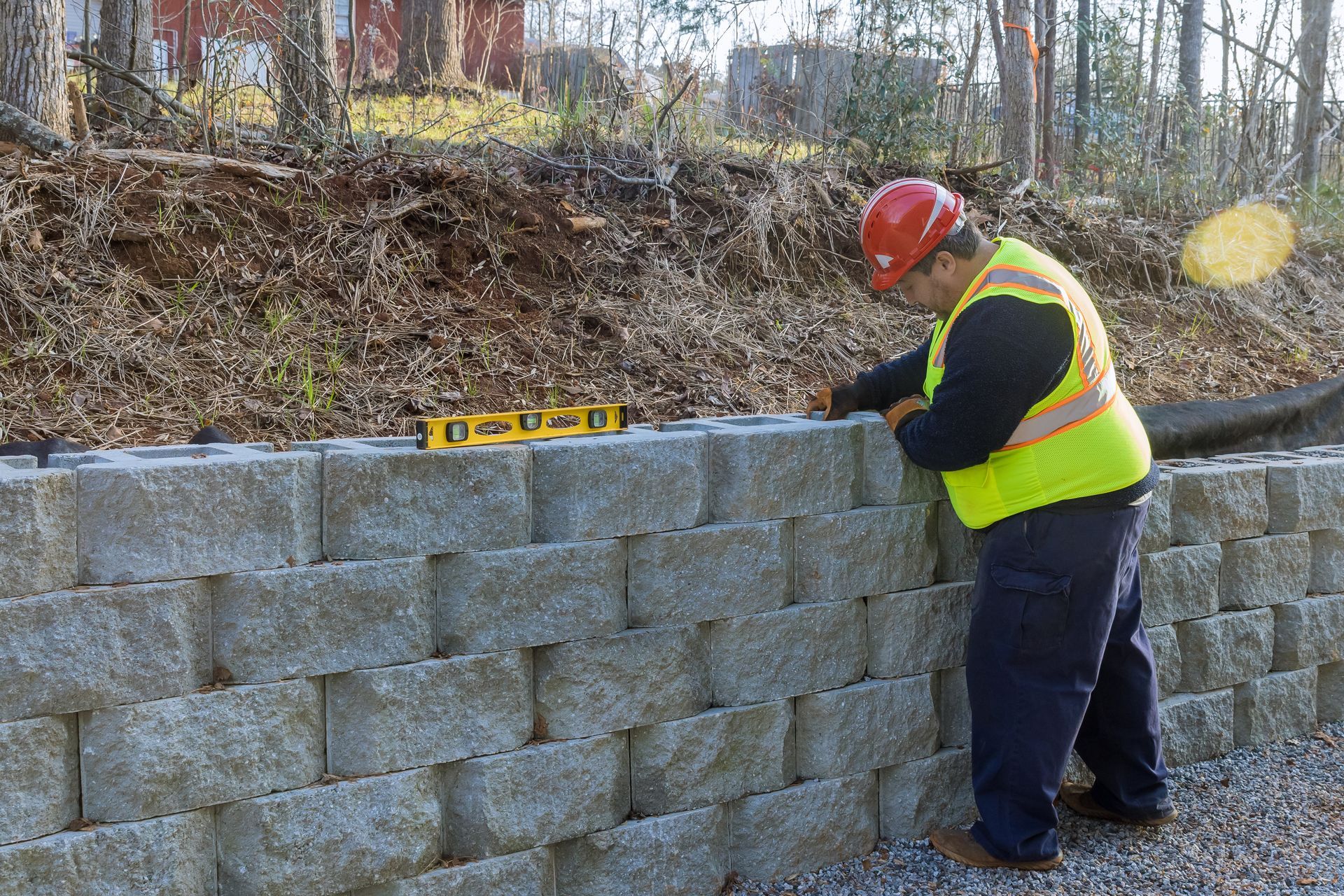 Worker in a hard hat measures a cinder block retaining wall at a construction site.