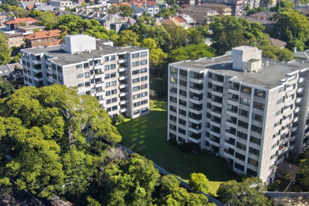 An aerial view of two tall buildings surrounded by trees in a city.
