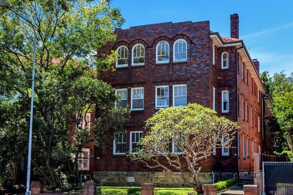 A large brick building with a lot of windows and trees in front of it.