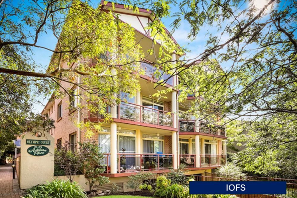 A large apartment building with lots of windows and balconies surrounded by trees.