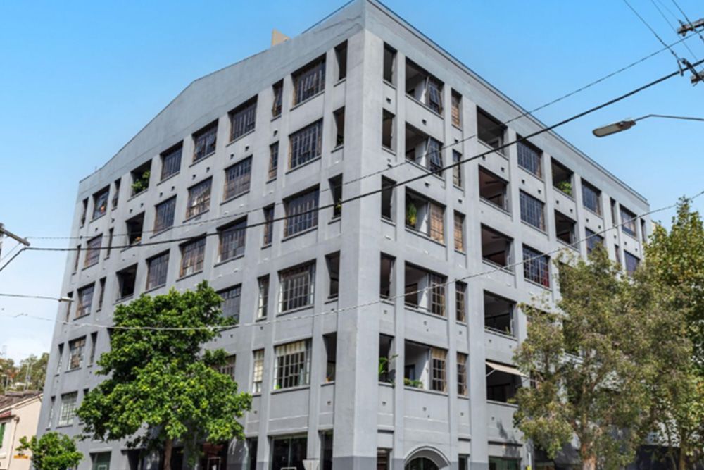 A large white building with a lot of windows is surrounded by trees and power lines.