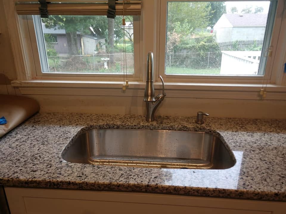 Kitchen sink beneath a window, with granite countertop and chrome faucet.
