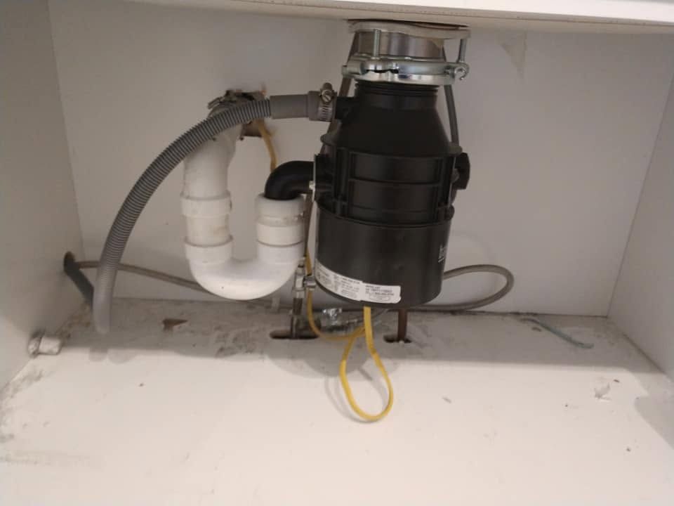 Under-sink garbage disposal and plumbing pipes inside a kitchen cabinet