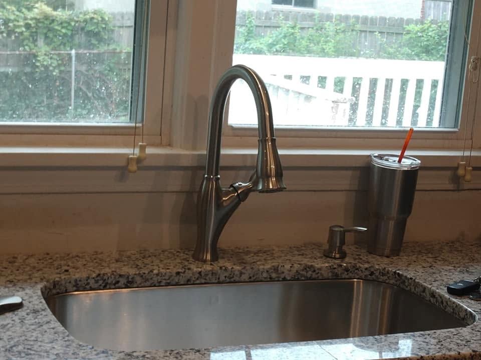Kitchen sink with stainless-steel faucet and soap dispenser on a granite countertop by a window