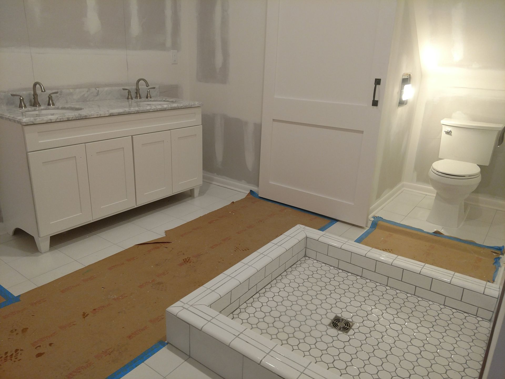 Bathroom under renovation with a white vanity, toilet, and shower floor drain exposed.