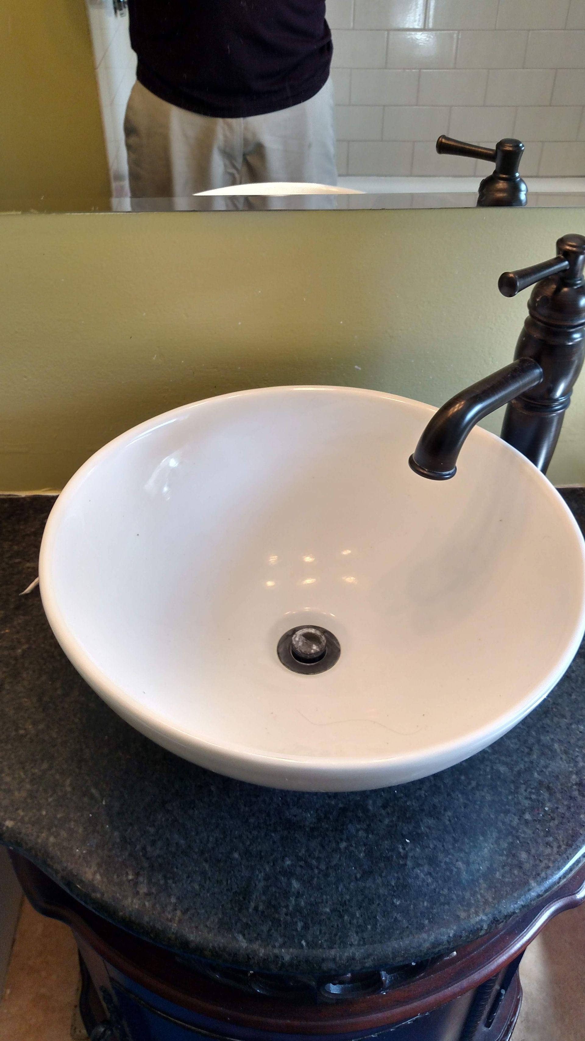 White vessel sink with black faucet on dark countertop in a bathroom, with a mirror showing a partial reflection.