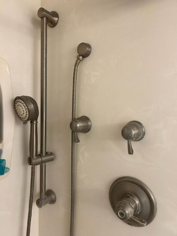 Shower stall with handheld showerhead, fixed showerhead, and control knobs on beige tile wall