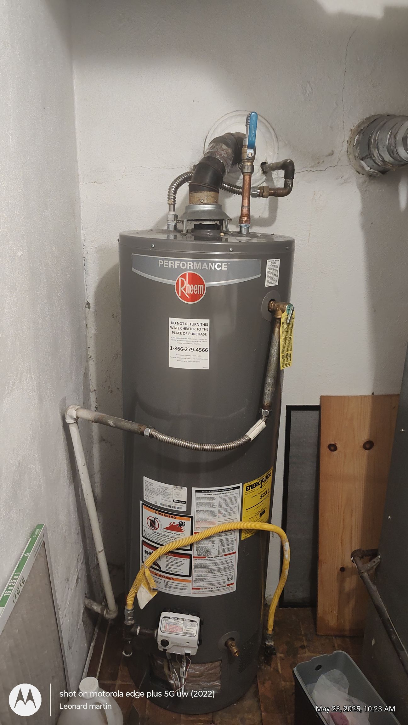 Gray water heater in a utility closet with pipes, yellow gas line, and a vent on top.