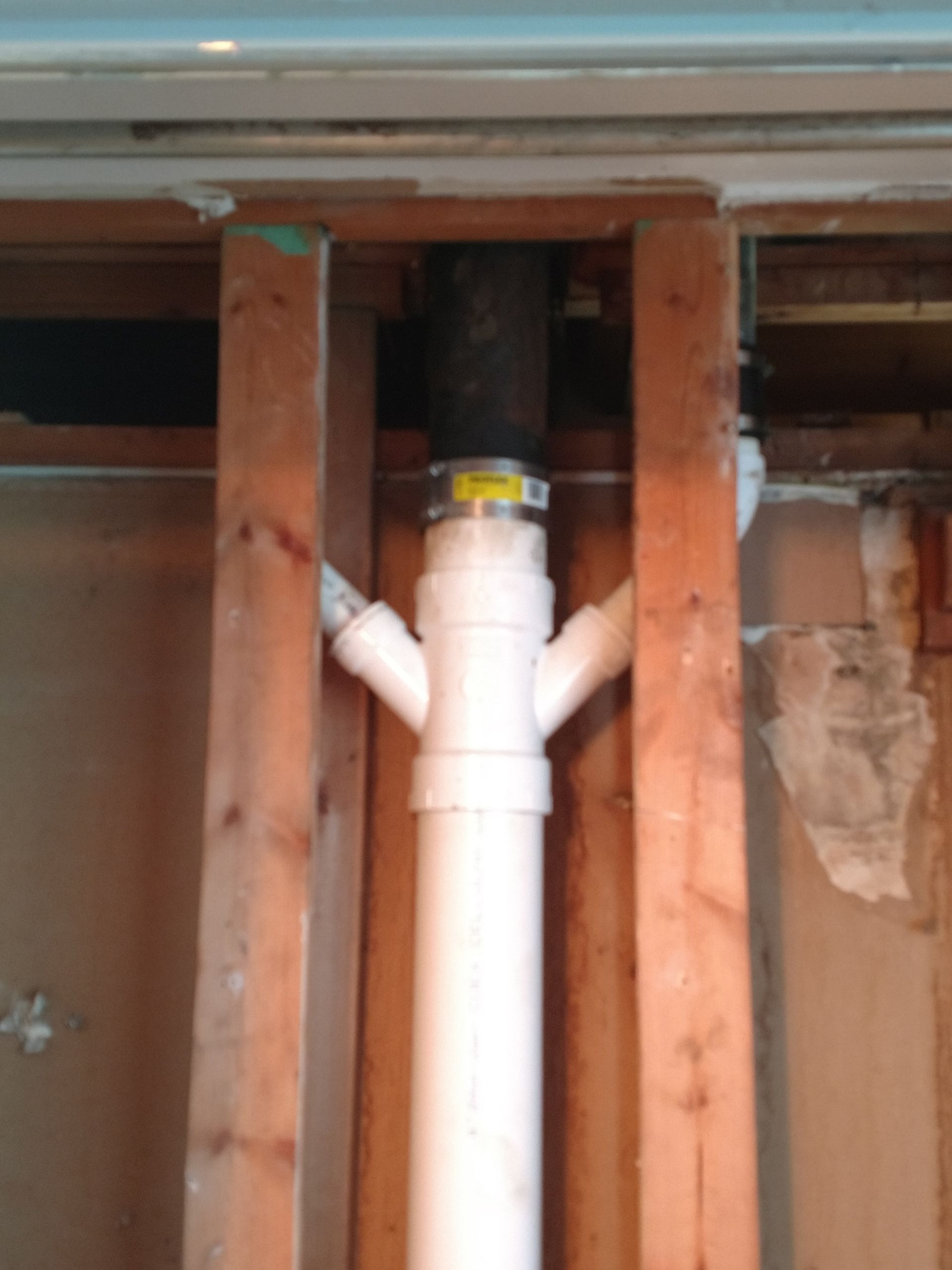 White PVC plumbing pipe with branches inside a wall cavity between exposed wooden studs.