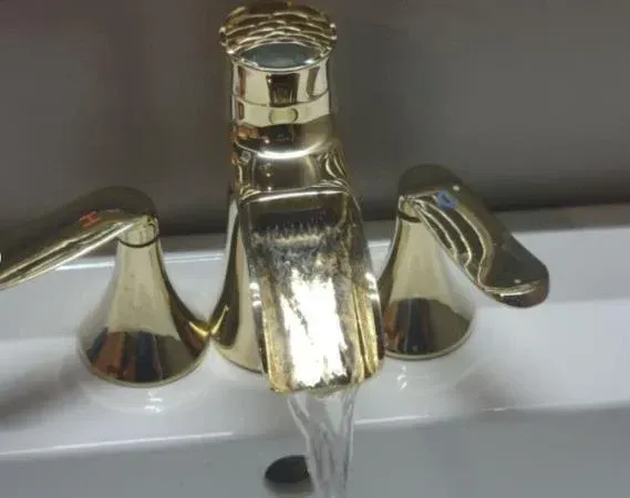 Gold bathroom faucet with water running into a white sink