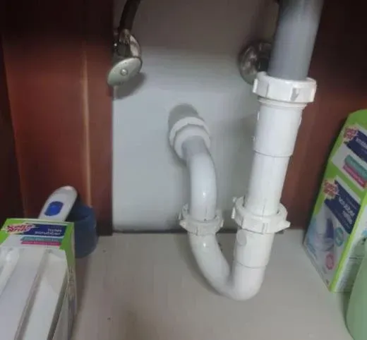 Under-sink plumbing with white PVC pipes and fittings inside a cabinet