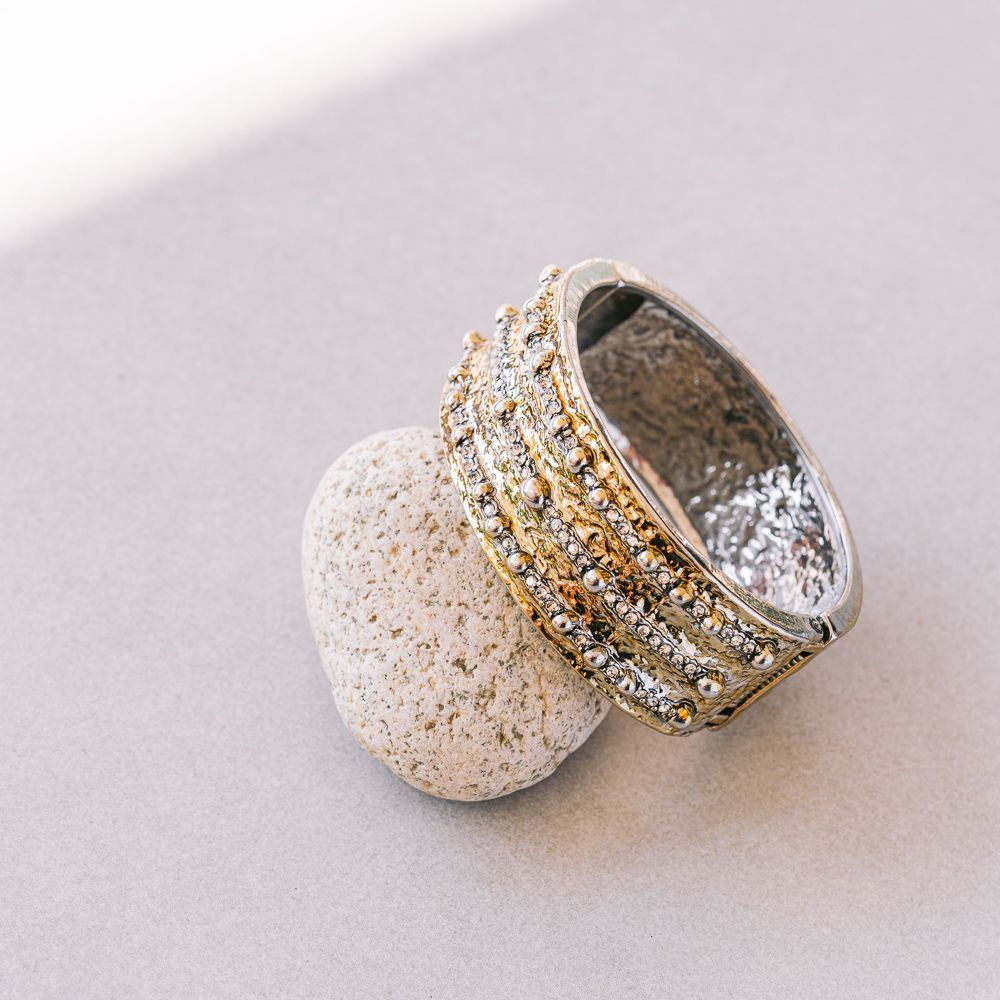 Anillo de plata con bandas apiladas de oro y diamantes que descansa sobre un pedestal de piedra blanca.