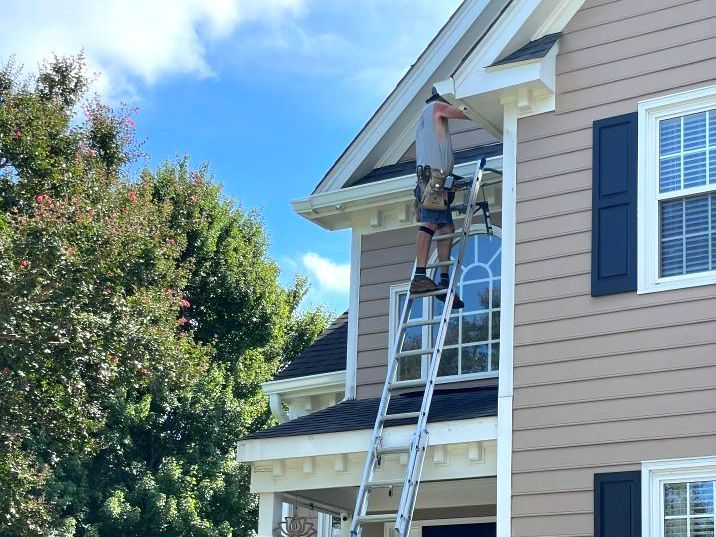 A man is standing on a ladder on the side of a house.