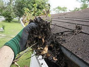a person is cleaning a gutter of leaves from a roof .