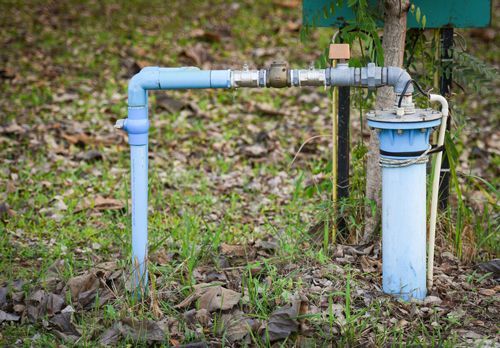 Blue water well piping with a filter in a grassy outdoor setting.