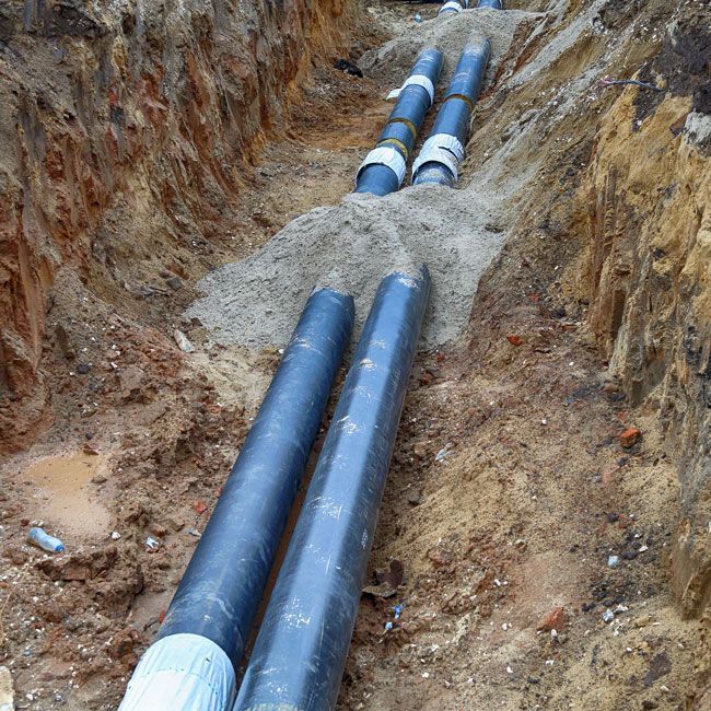Pipes in a trench. Black pipes wrapped in white tape lie in a dirt trench, likely for underground utilities.