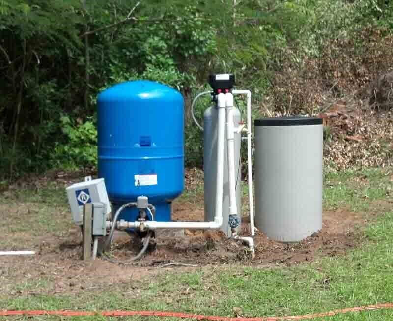 Outdoor well water system with blue tank, filtration, and grey holding tank.