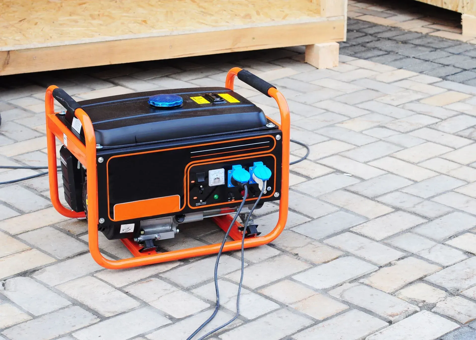 A portable orange and black generator sitting on a paved surface with power cords plugged into it.