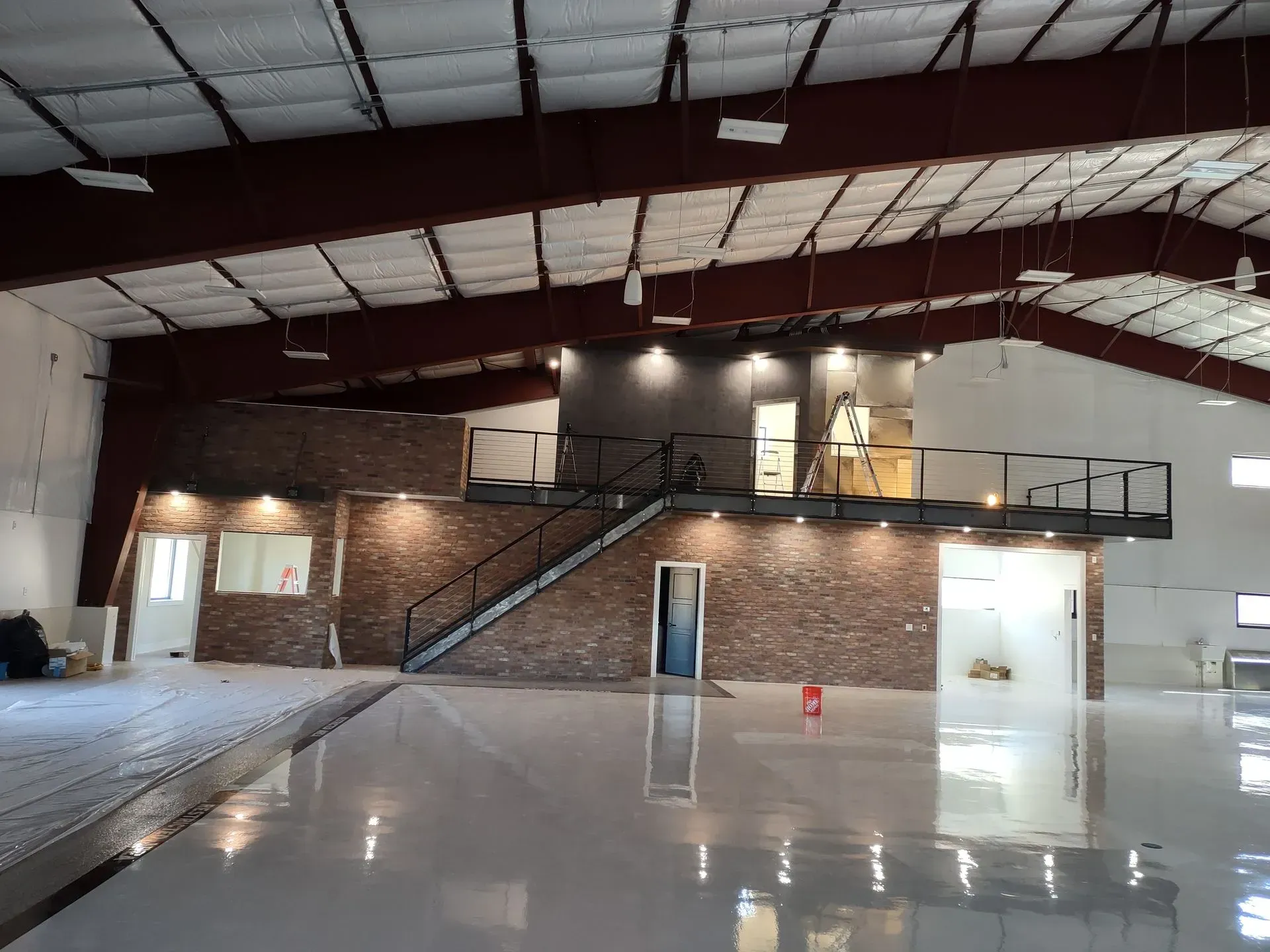 A wide view of a spacious warehouse interior with a stone-accented mezzanine, staircase, and polished reflective floors.