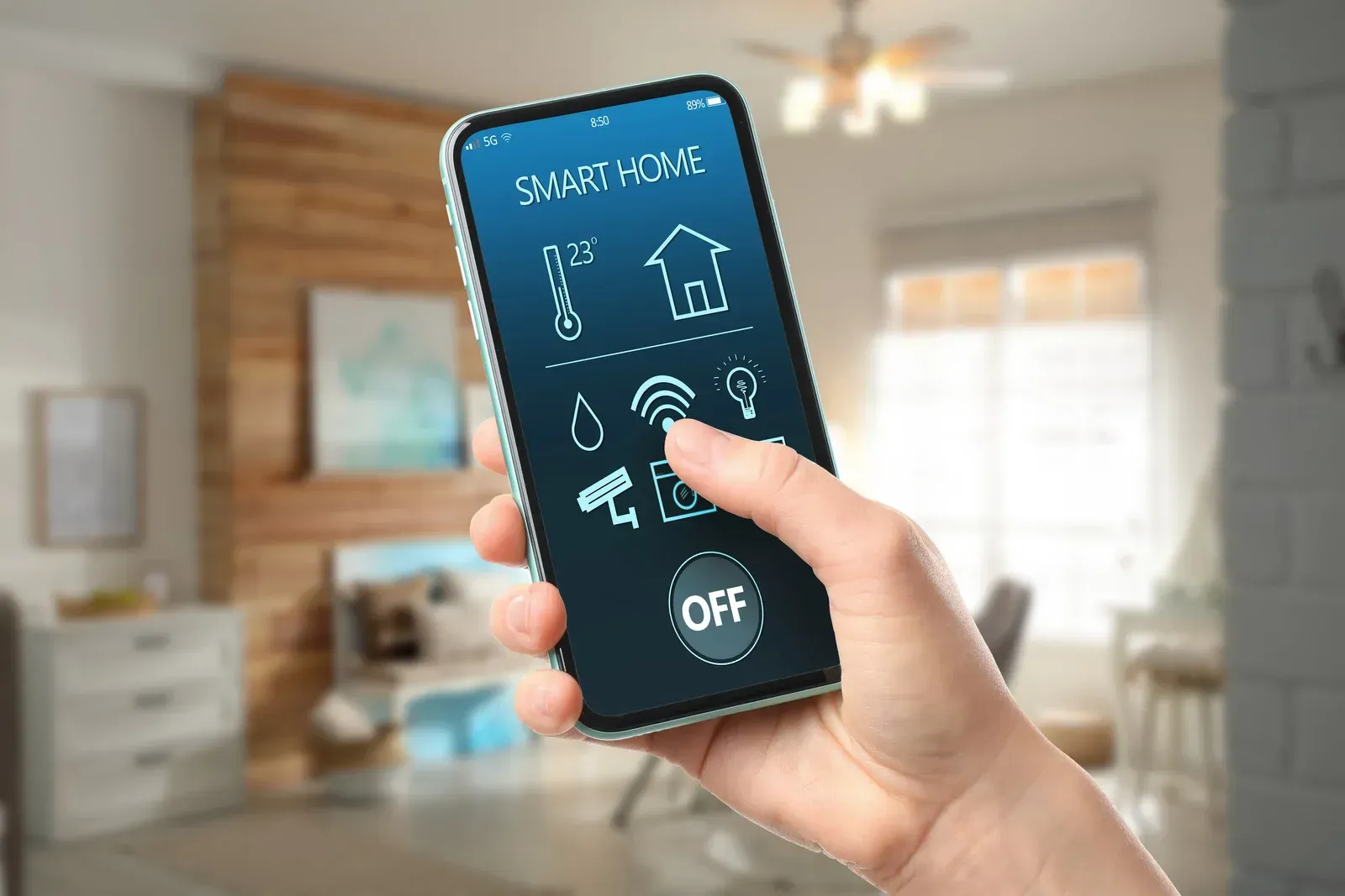 A hand holding a smartphone displaying a smart home control app against a blurred home interior background.