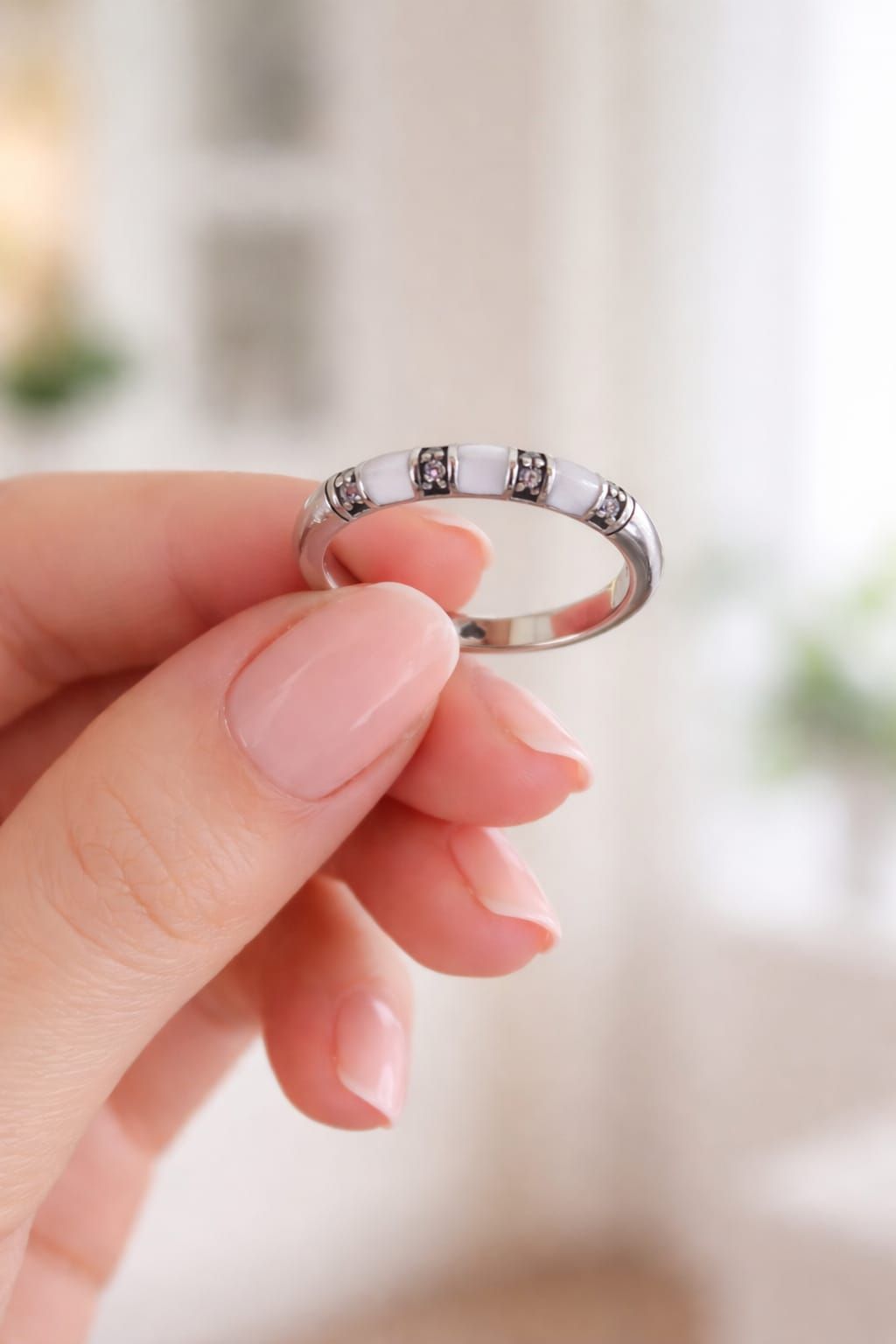 Mano con un anillo de plata con pequeñas piedras transparentes sobre un fondo claro difuminado.
