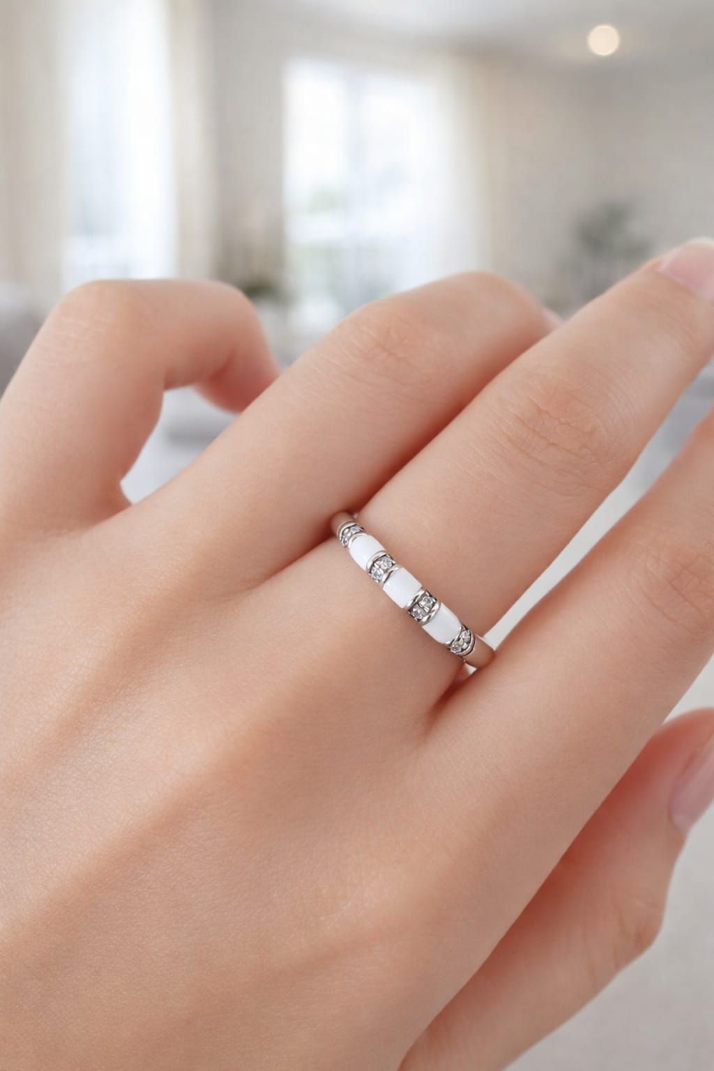 Mano con un anillo de plata con pequeñas piedras transparentes sobre un fondo claro difuminado.
