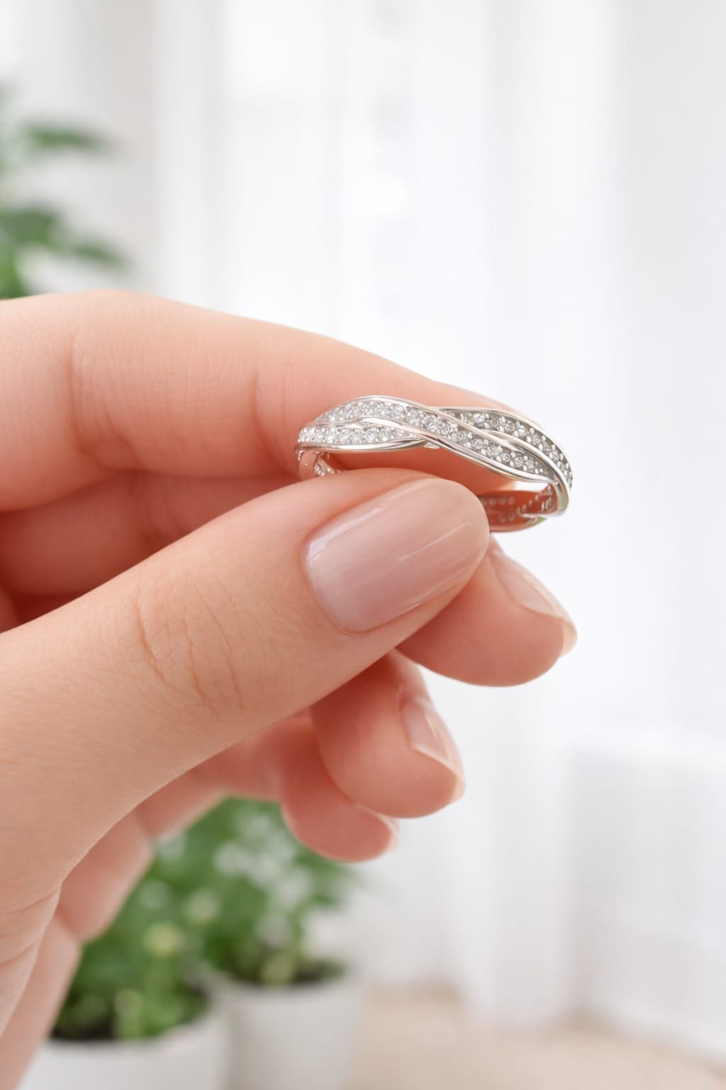Mano con un anillo de plata con pequeñas piedras brillantes sobre un fondo blanco suave.
