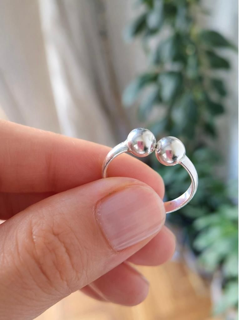 Una mano con un anillo de plata y una piedra preciosa transparente descansa sobre un fondo suavemente difuminado.